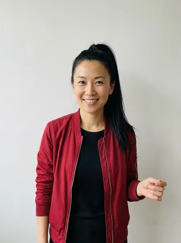 Photo of a woman in a red bomber jacket who sings backup on the right in an Outstanding Tiny Desk video